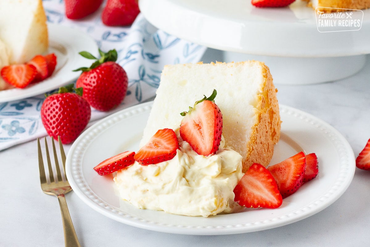 Slice of Angel Food Cake with pineapple whip topping and fresh sliced strawberries on a plate.