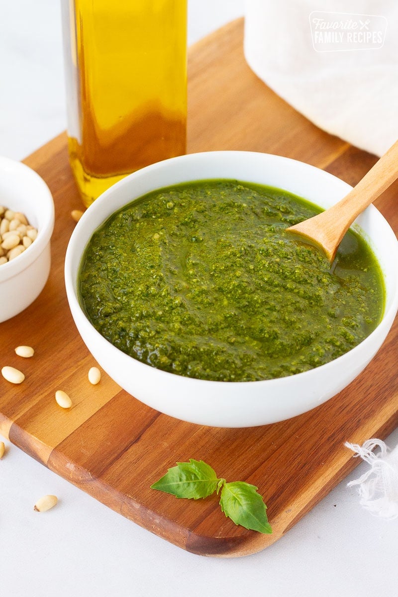 Bowl of Homemade Pesto with a spoon. Olive oil, pine nuts and fresh basil on the side.