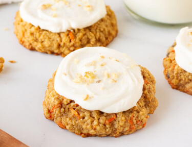 Three Carrot Cake Cookies topped with Cream Cheese Frosting and sprinkled with chopped walnuts. Milk on the side.