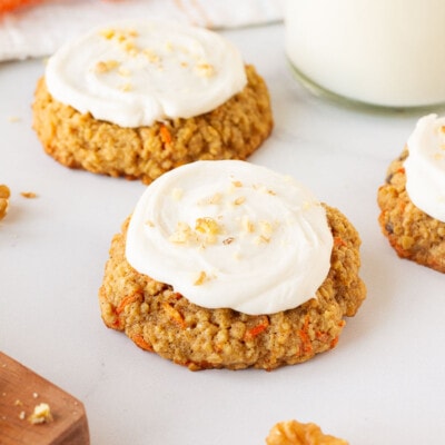 Three Carrot Cake Cookies topped with Cream Cheese Frosting and sprinkled with chopped walnuts. Milk on the side.