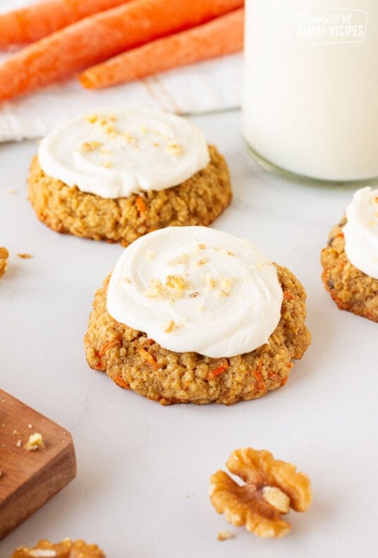 Three Carrot Cake Cookies topped with Cream Cheese Frosting and sprinkled with chopped walnuts. Milk on the side.