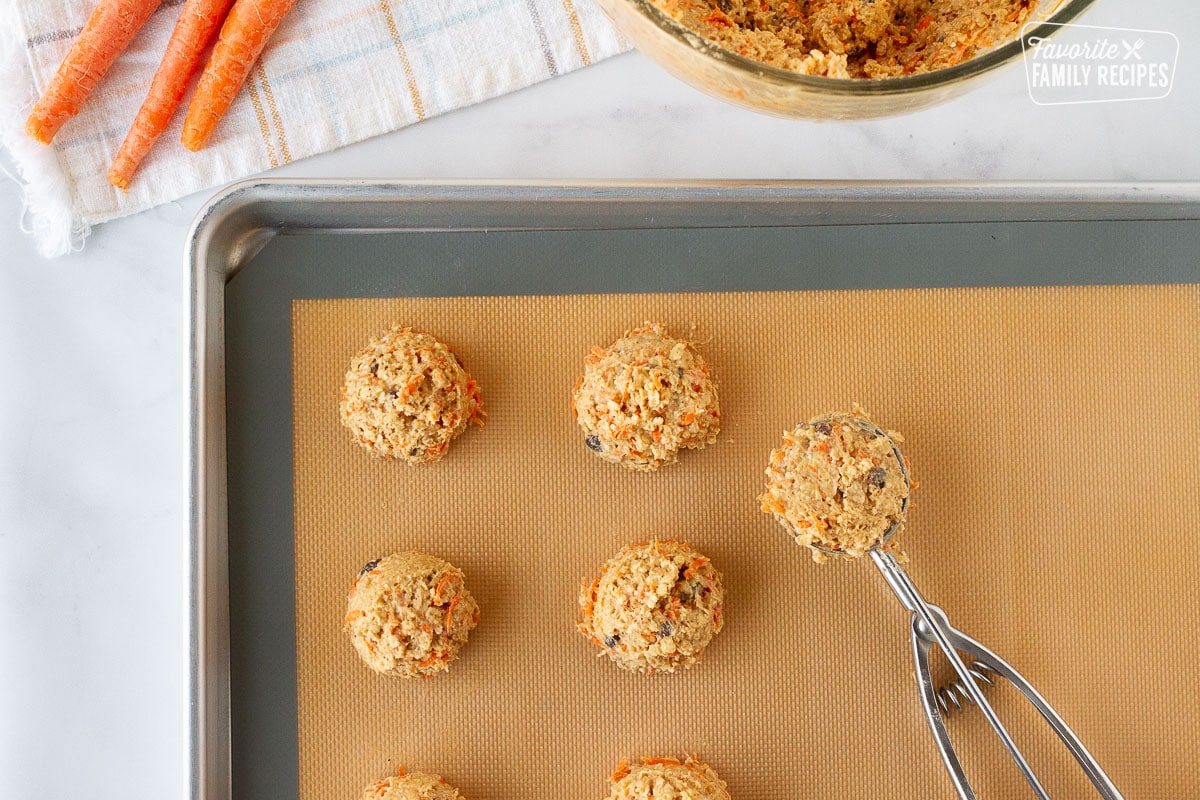 Scooped Carrot Cake Cookies on a cookie sheet with a baking mat and cookie scoop.