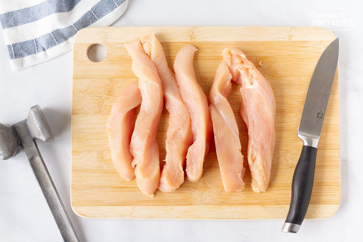 Chicken breads flattened and cut into strips on a cutting board with a knife and mallet for Applebee's Oriental Chicken Salad.