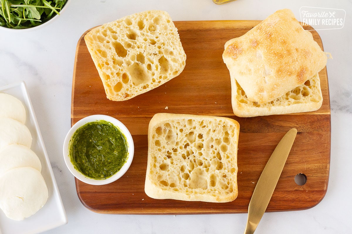 Cutting board with ciabatta bread and pesto mayo for Chicken Pesto Sandwiches.