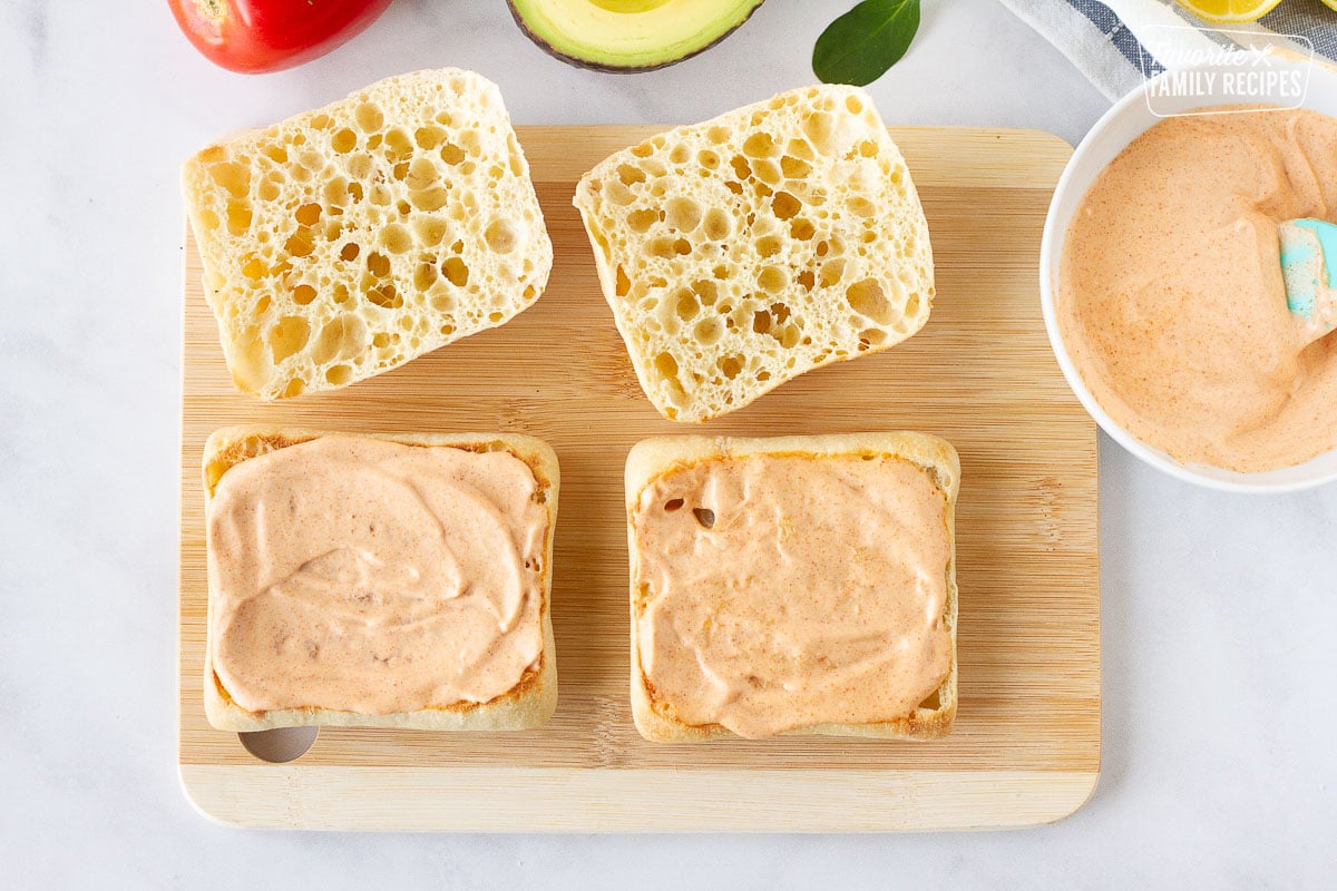 Cutting board with two ciabatta bread topped with spicy aioli sauce for Grilled Chicken Sandwiches.