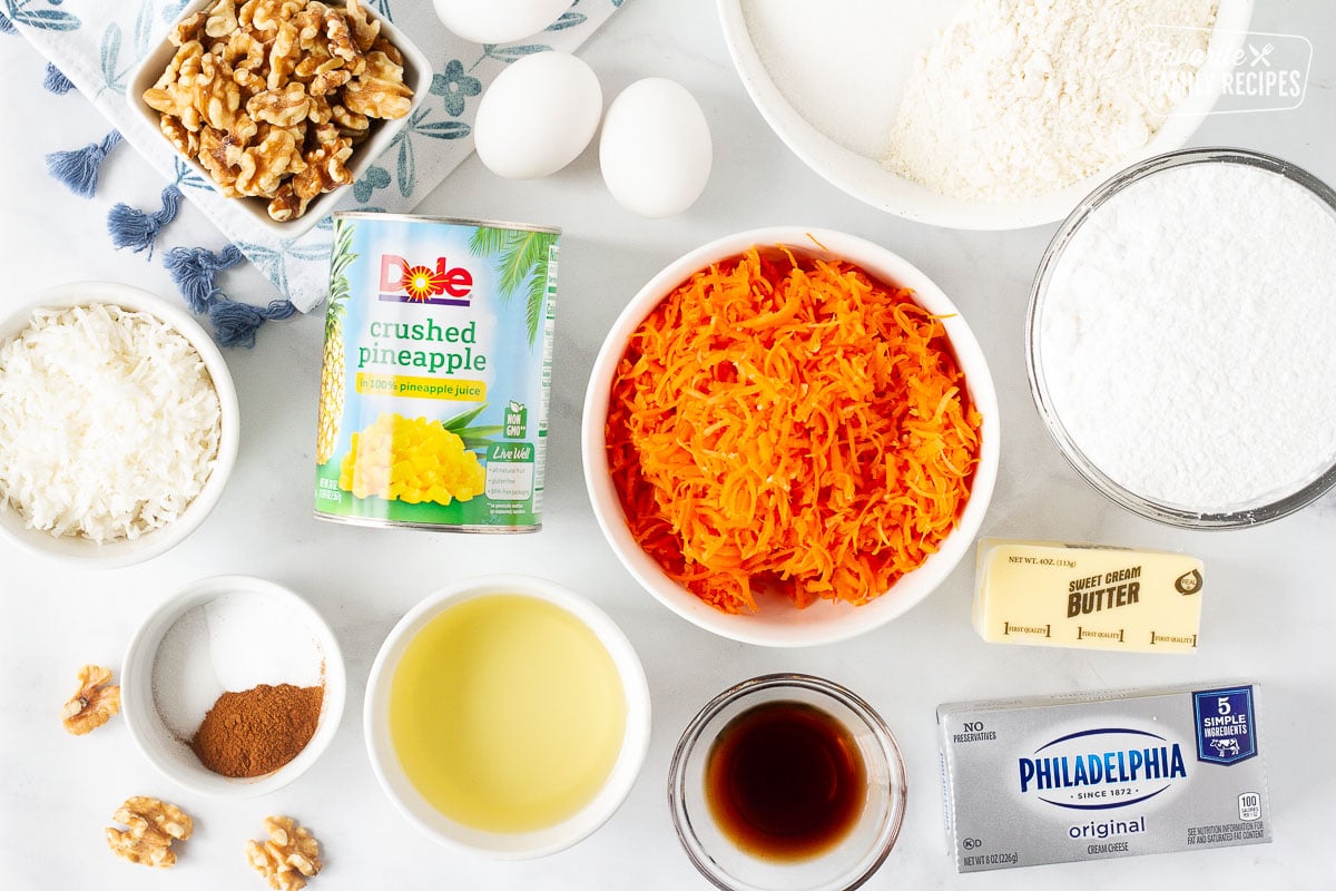 Classic Carrot Cake ingredients including shredded carrots, crushed pineapple, walnuts, coconut, spices, oil, vanilla, eggs, flour, sugar, cream cheese and butter.