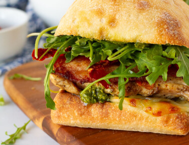One Chicken Pesto Sandwich on ciabatta bread with bacon, sun-dried tomatoes and arugula.