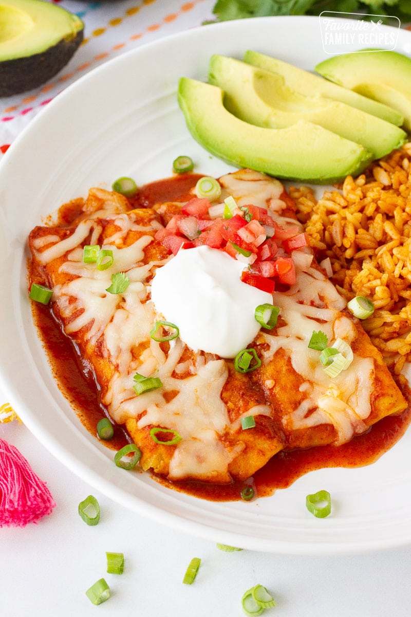 Plate of Easy Cheese Enchiladas with rice, avocado and sour cream on top.