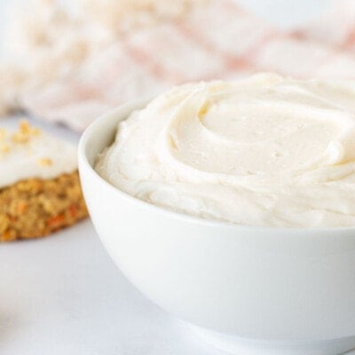 Bowl of Cream Cheese Frosting next to cookies topped with Cream Cheese Frosting.