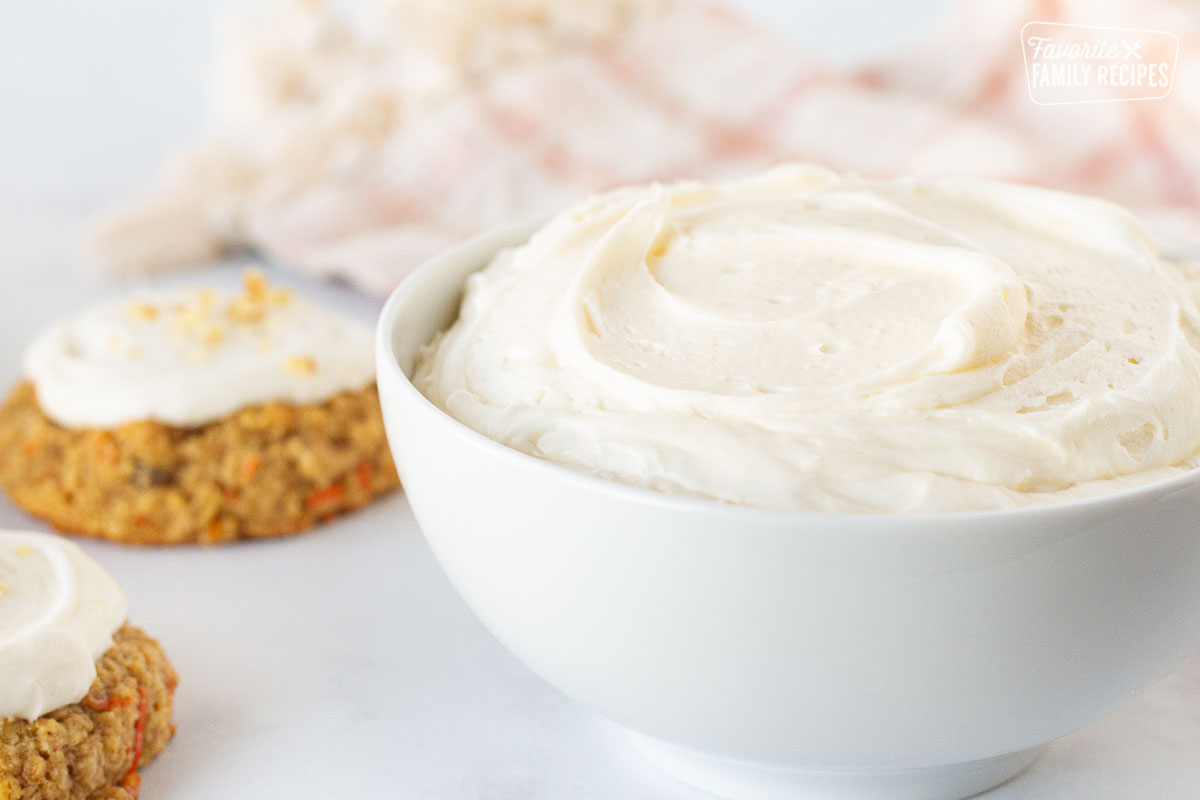 Bowl of Cream Cheese Frosting next to cookies topped with Cream Cheese Frosting.