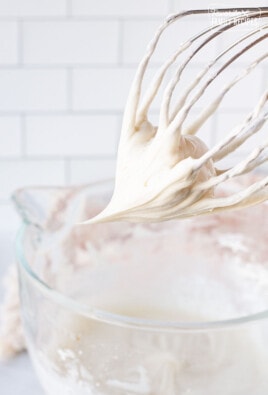 Mixing whisk with Cream Cheese Frosting over a mixing bowl.