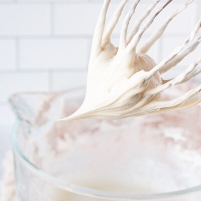 Mixing whisk with Cream Cheese Frosting over a mixing bowl.