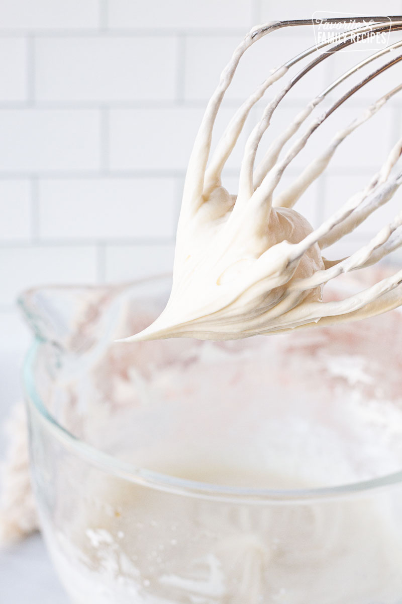 Mixing whisk with Cream Cheese Frosting over a mixing bowl.