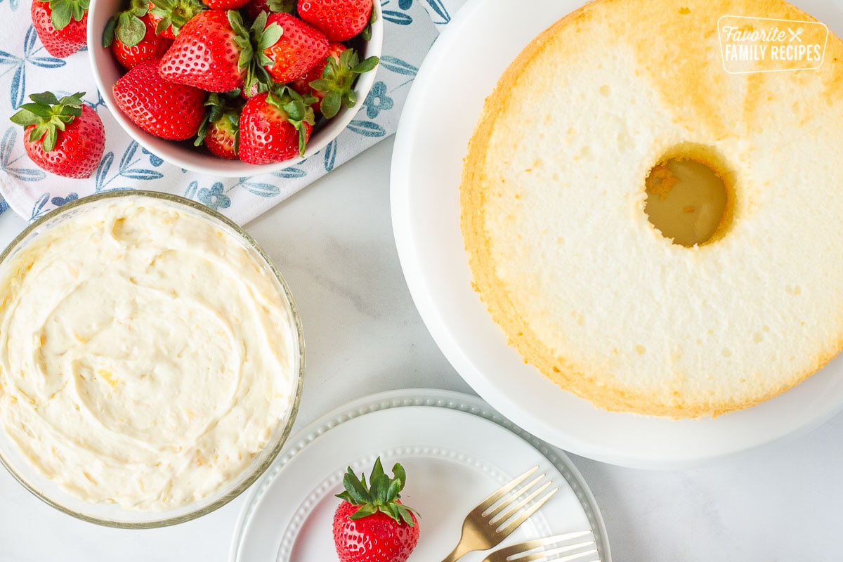 Baked Angel Food Cake, bowl of pineapple whipped topping, bowl of fresh strawberries and plates with forks.