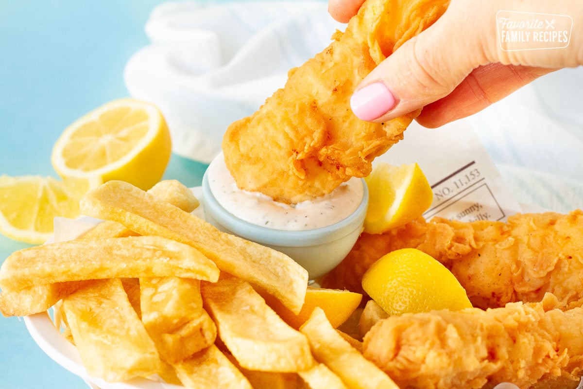 Hand dipping Fish and Chips into tartar sauce.