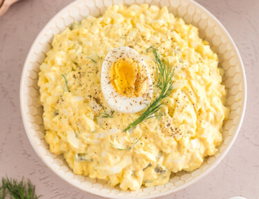 Egg salad in a bowl topped with half of a hard boiled egg and a sprig of dill