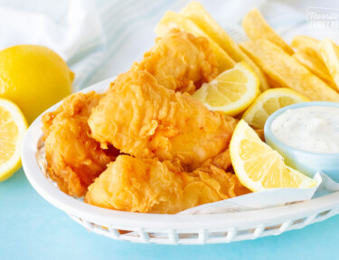 Three fillets of Fish and Chips in a basket with lemon wedges and tartar sauce.