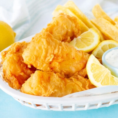 Three fillets of Fish and Chips in a basket with lemon wedges and tartar sauce.