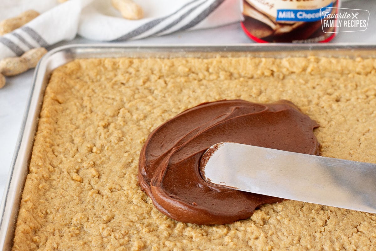 Spreading milk chocolate frosting with a spatula on top of baked Peanut Butter Bars.
