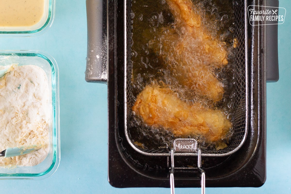 Battered fish in a deep fryer for Fish and Chips next to the bowls of batter and flour.