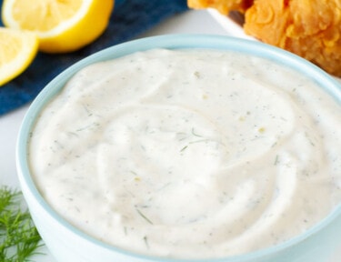 Bowl of Homemade Tartar Sauce in front of a plate of battered fish and lemon.