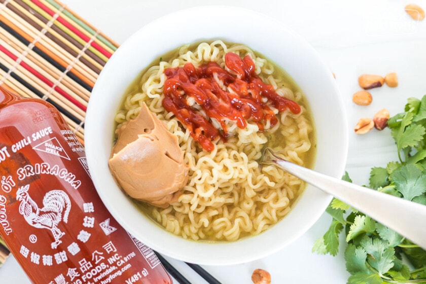 A bowl of ramen noodles with a scoop of peanut butter and sriracha over the top.