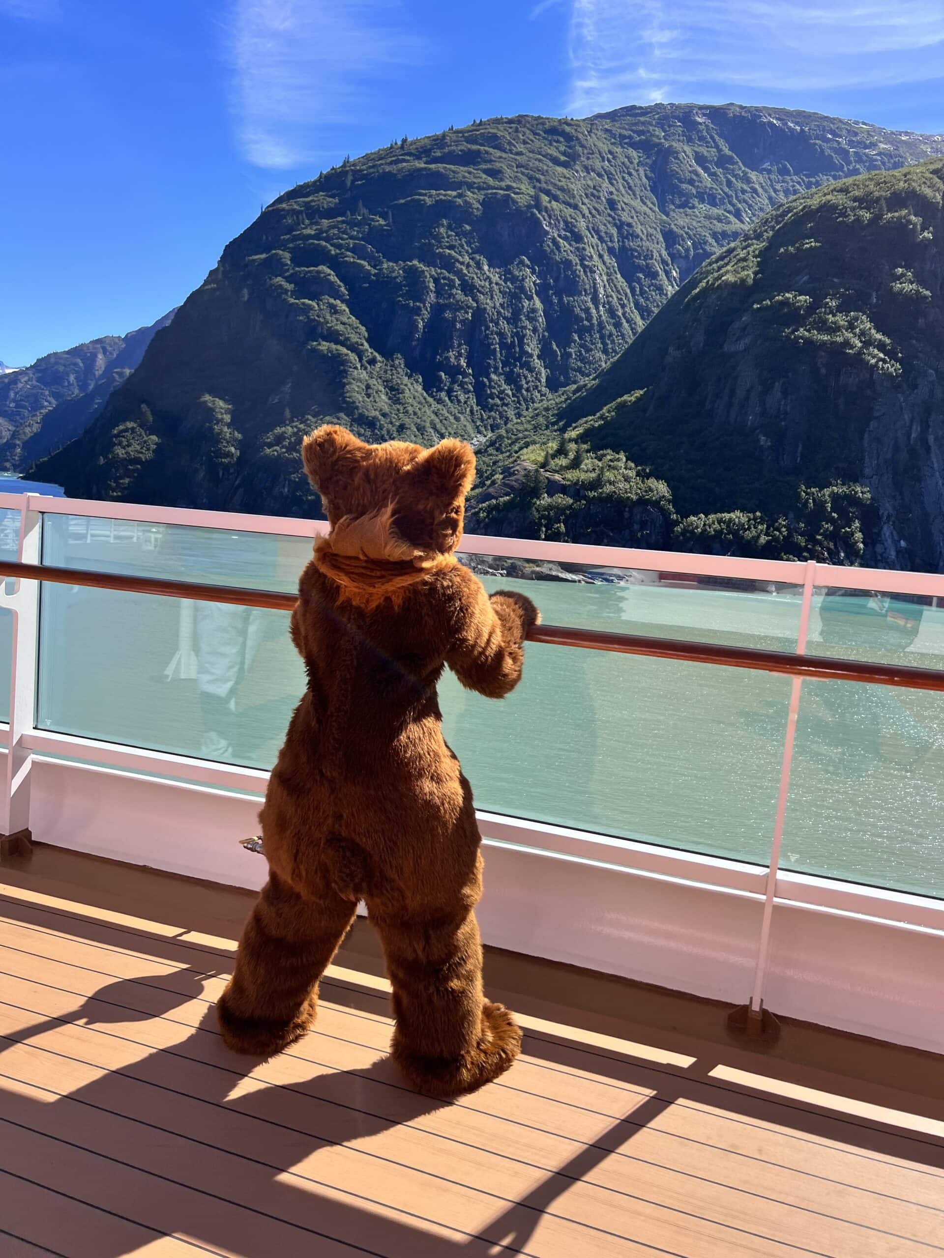 A costumed bear looking over the side of the Disney Wonder at the mountains in Alaska.