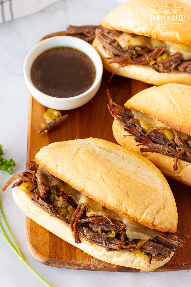Three Italian Beef Sandwiches lined up with au jus dipping sauce.
