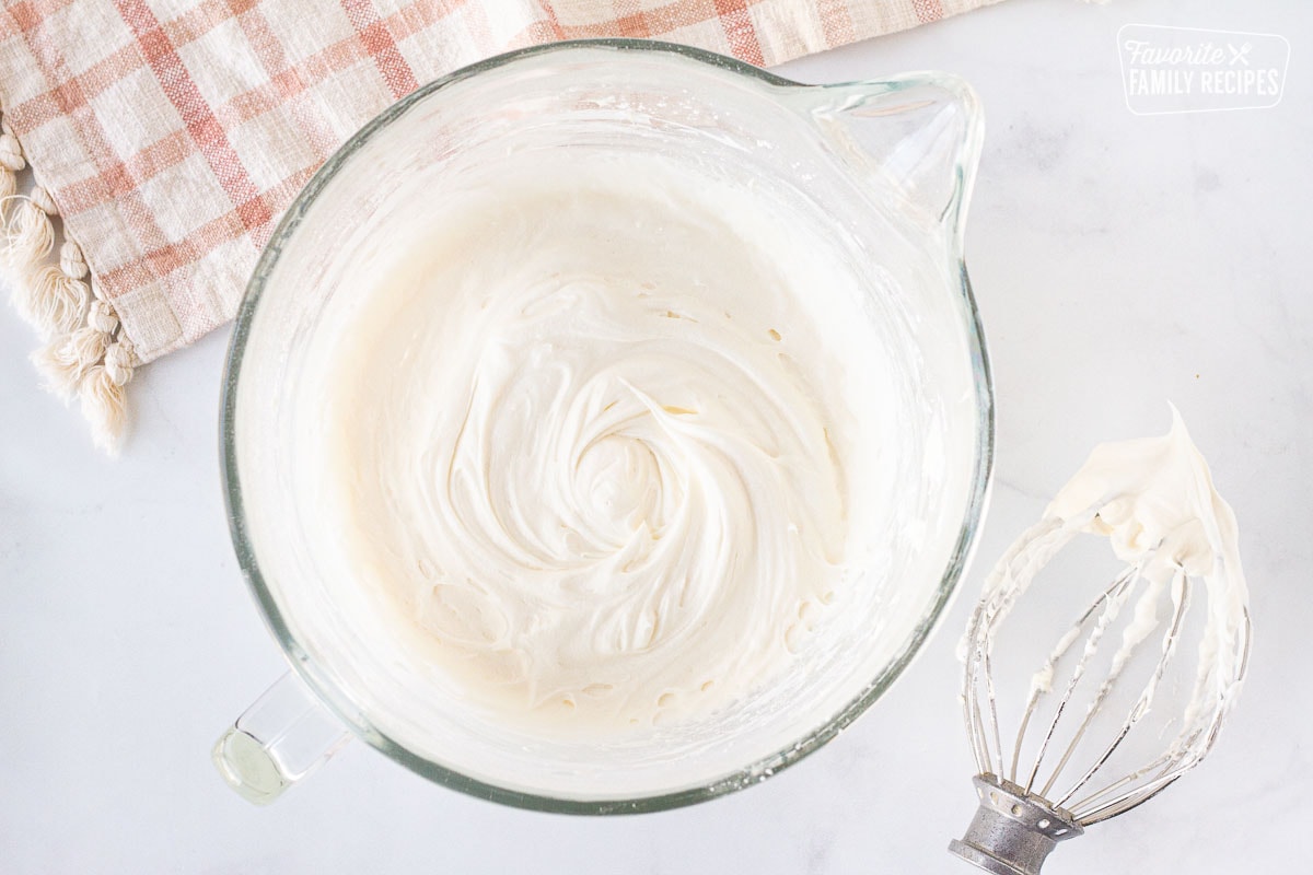 Mixing bowl with Cream Cheese Frosting with a mixing whisk on the side.