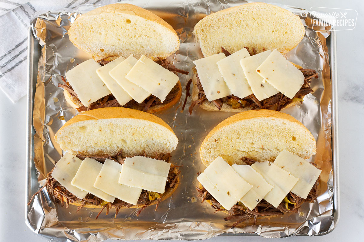 Four rolls with beef and pepper jack cheese on a baking sheet for Italian Beef Sandwiches.