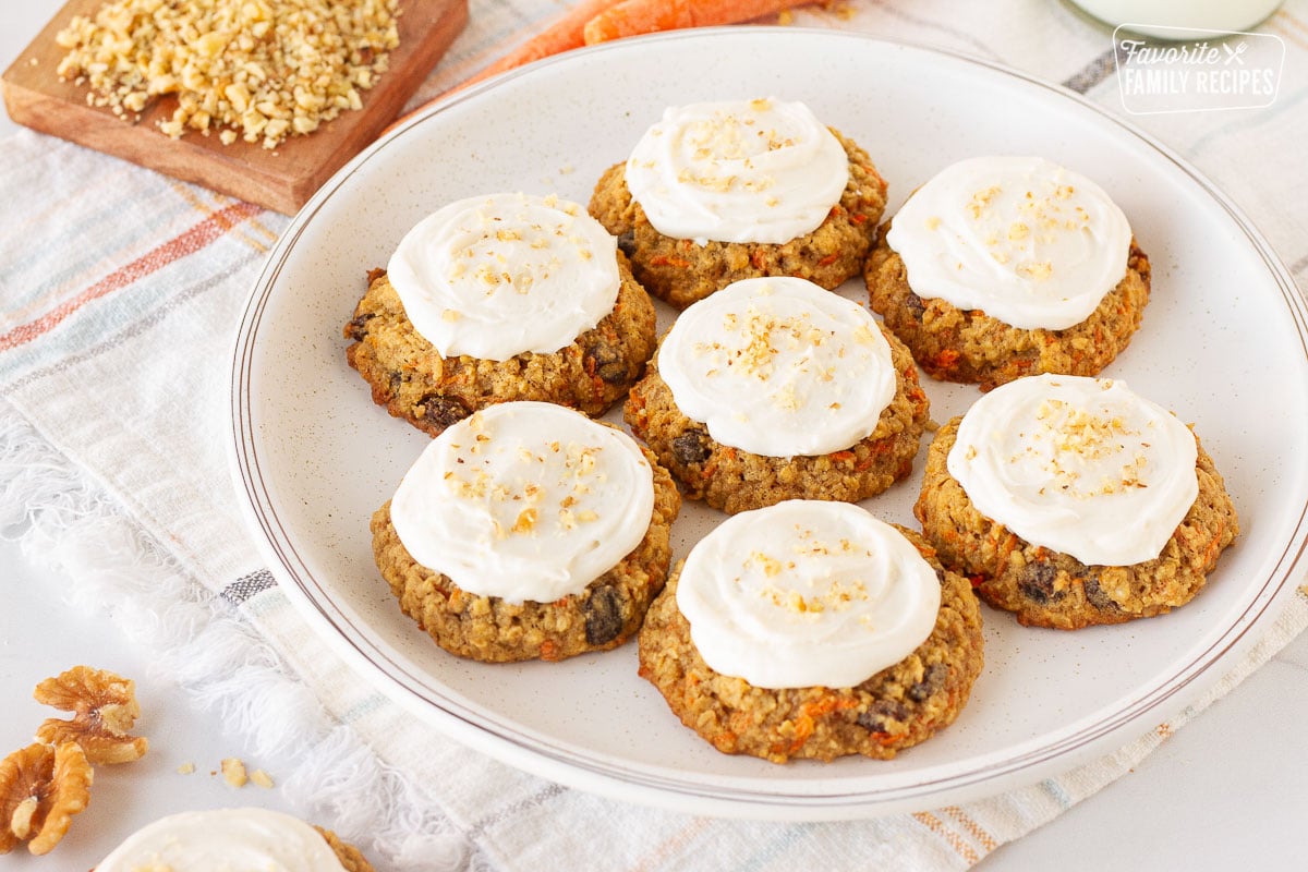 Side view of seven Carrot Cake Cookies on a plate frosted with cream cheese frosting and sprinkled with chopped walnuts.