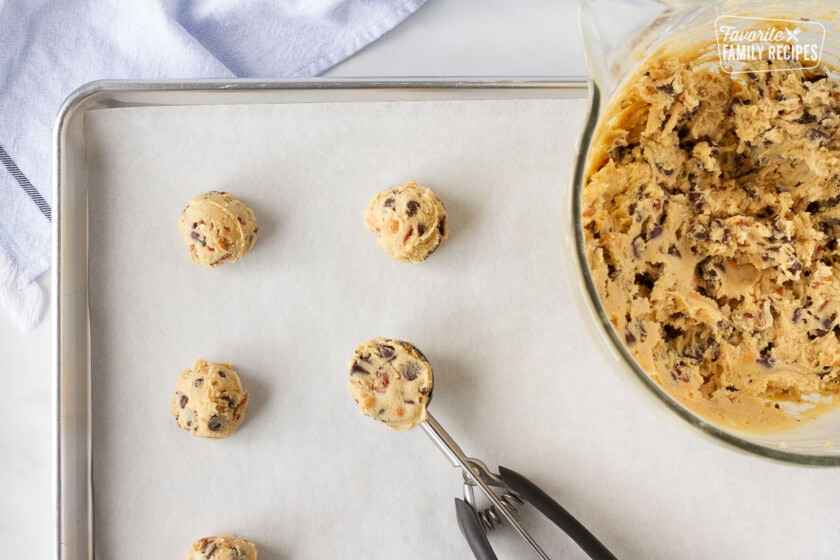 Cookie sheet with Turtle cookie balls, cookie scoop and mixing bowl of cookie dough.