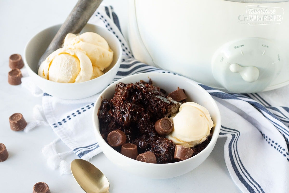 Bowl of Crockpot Lava Cake next to the Crockpot and ice cream bowl with scoop.