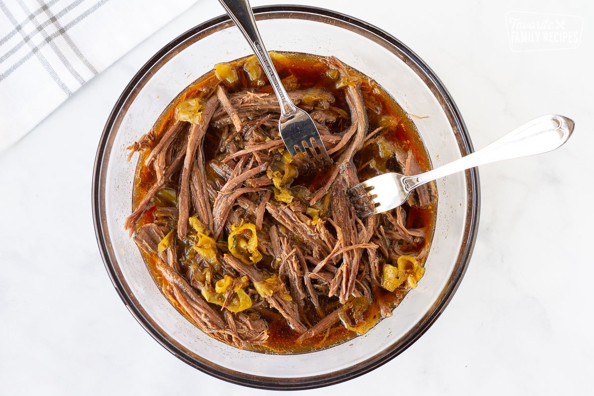 Bowl of Shredded beef roast with juices for Italian Been Sandwiches. Two forks in the bowl for shredding.