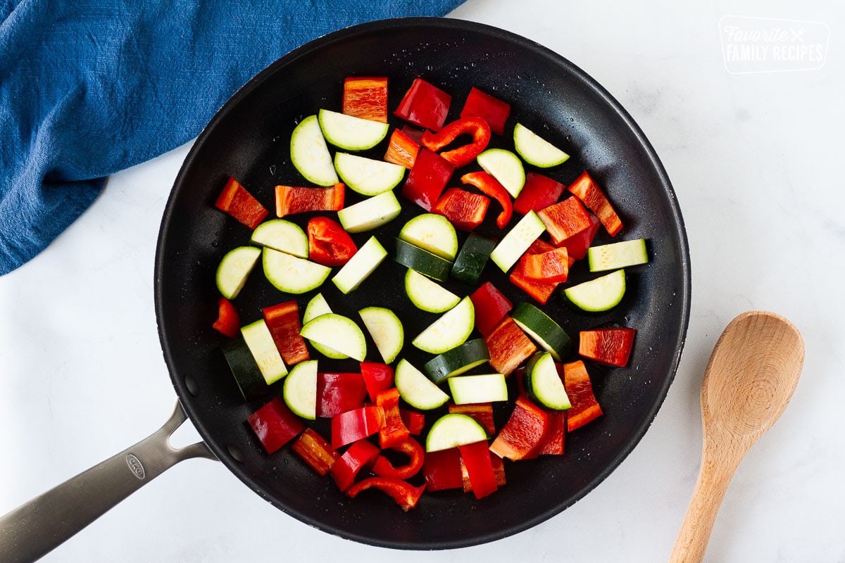 Chopped red peppers and zucchini in a skillet for Kung Pao Chicken. Wooden spoon on the side.
