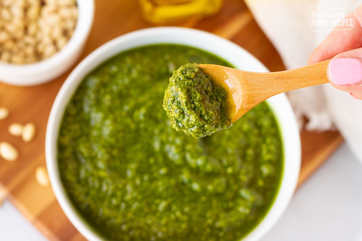 Hand holding a wooden spoon full of Homemade Pesto.