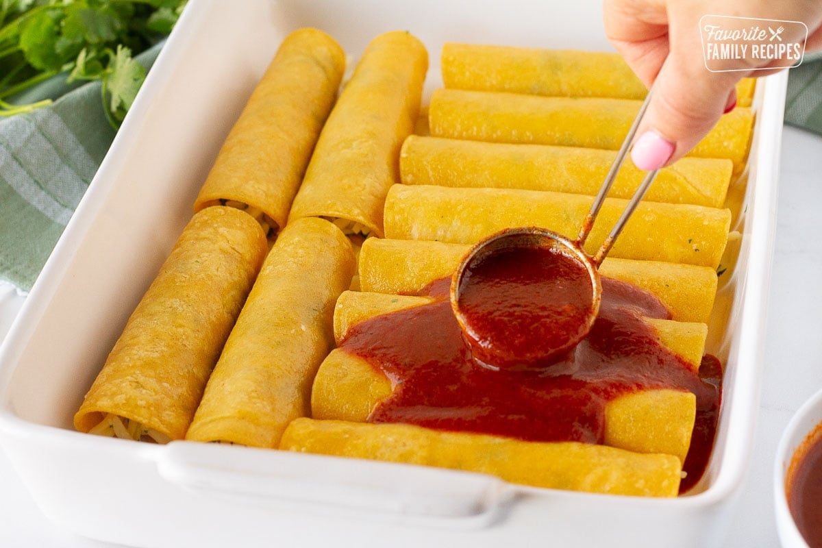 Ladling Homemade Enchilada Sauce over a dish of corn tortilla cheese enchiladas.