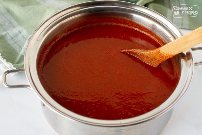 Wooden spoon stirring simmering Homemade Enchilada Sauce.