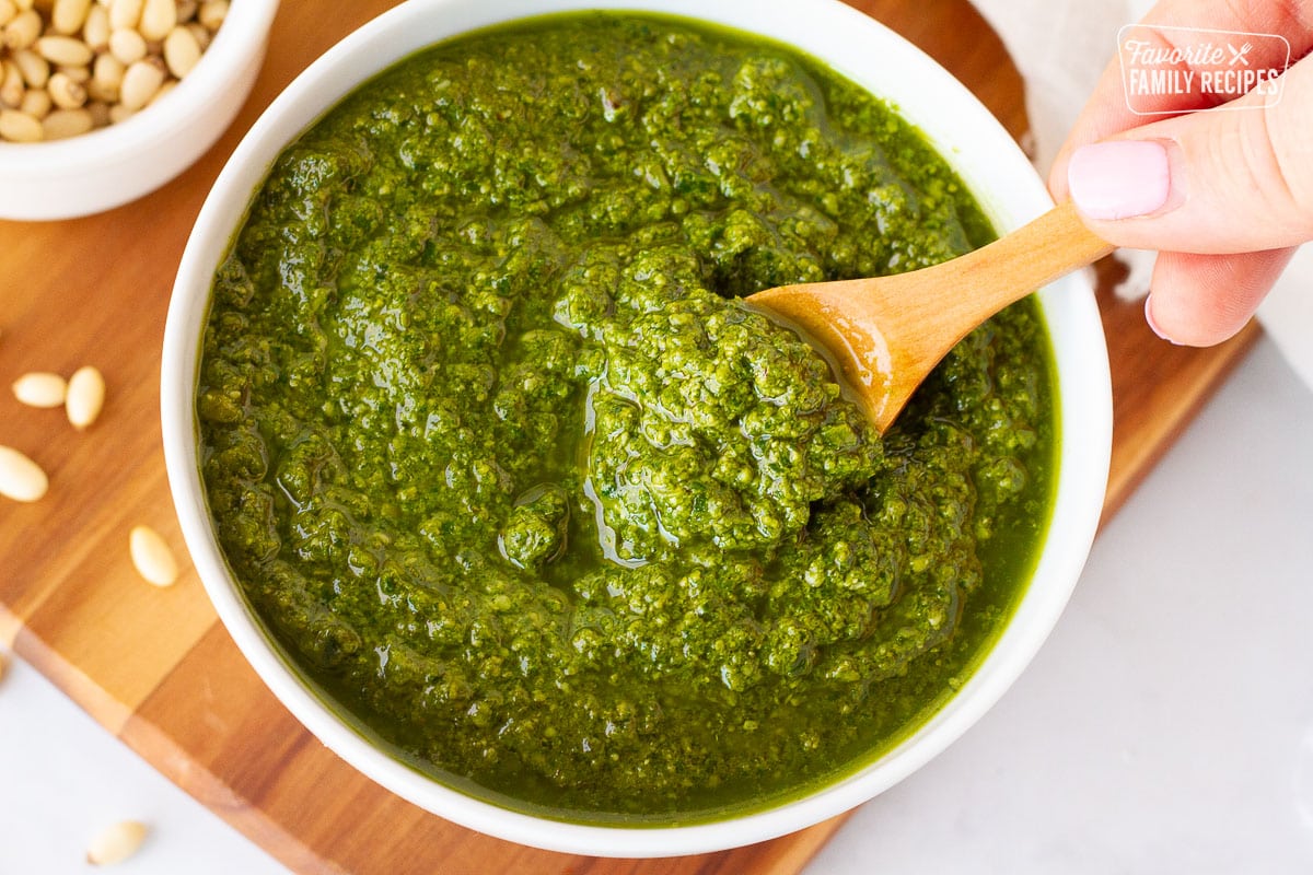 Hand stirring Homemade Pesto in a bowl with a wooden spoon.