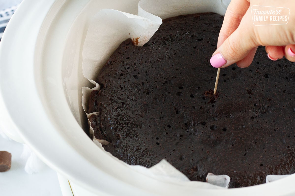 Hand poking toothpick in the center of the baked Crockpot Lava Cake.