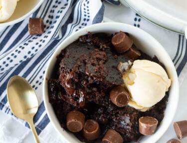 Crockpot Lava Cake in a bowl with ice cream and Rolo chocolate candies. Vanilla ice cream scoops on the side.