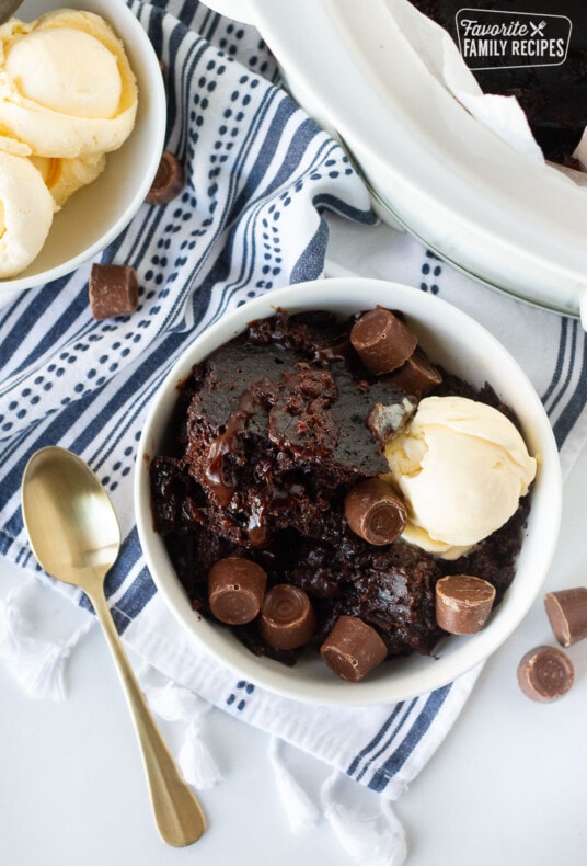 Crockpot Lava Cake in a bowl with ice cream and Rolo chocolate candies. Vanilla ice cream scoops on the side.