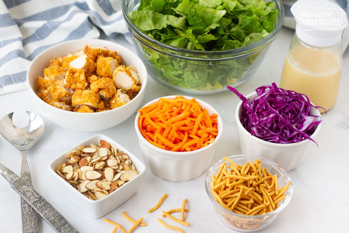 Bowls of lettuce, cut up chicken, carrots, almonds, red cabbage, rice noodles and salad dressing for Applebee's Oriental Chicken Salad.