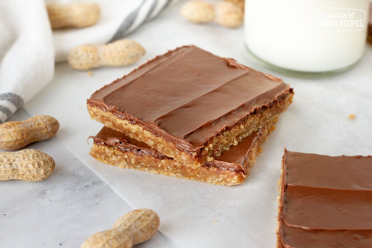 Two Peanut Butter Bars stacked together. Milk and peanuts on the side.