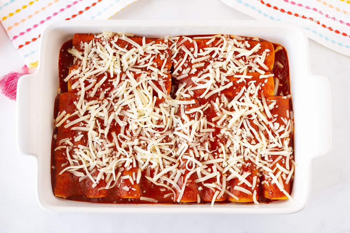 Pan of unbaked Easy Cheese Enchiladas with sauce and cheese on top.