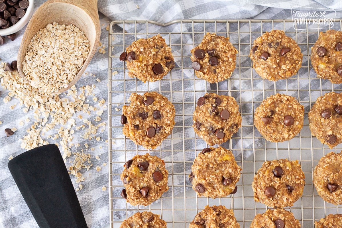 Baked Healthy Oatmeal Cookies on a cooling rack. Oats, chocolate chips and spatula on the side.
