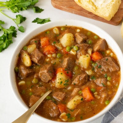Hearty Beef Stew in a bowl with a spoon. Buttered dinner roll on the side.