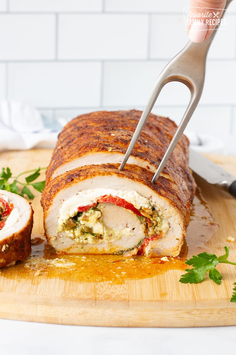 Fork piercing into a slice of Stuffed Pork Loin on a cutting board.