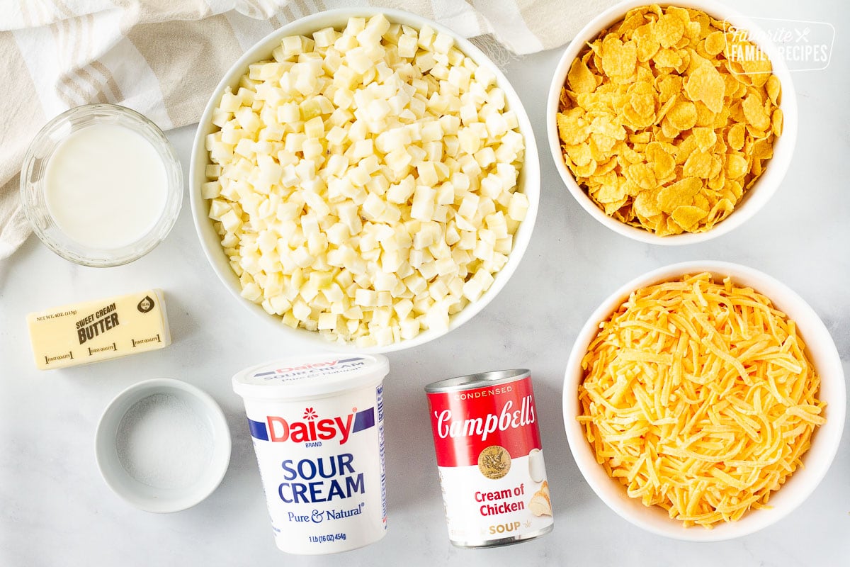 Ingredients for Cheese Potato Casserole including cream of chicken soup, sour cream, potatoes, corn flakes, cheese, butter, salt and milk.