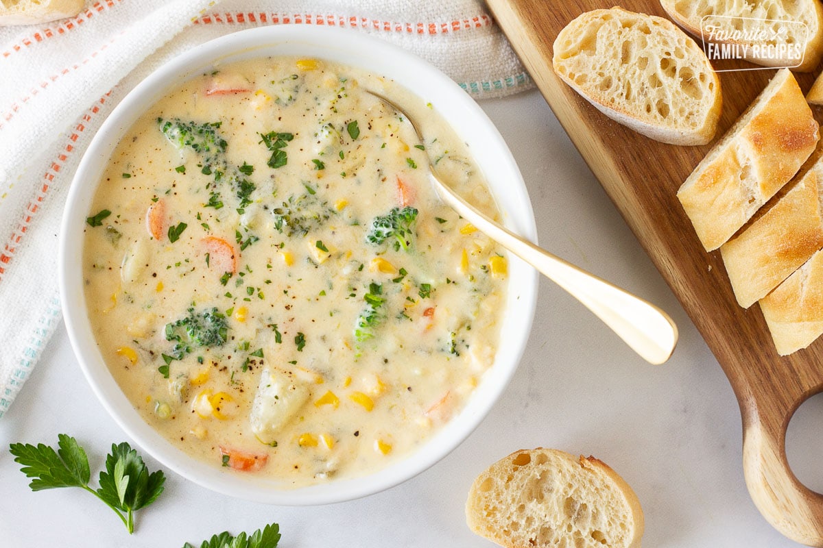 Bowl of Creamy Vegetable Soup with parsley and pepper for garnish. Cutting board of sliced bread on the side.